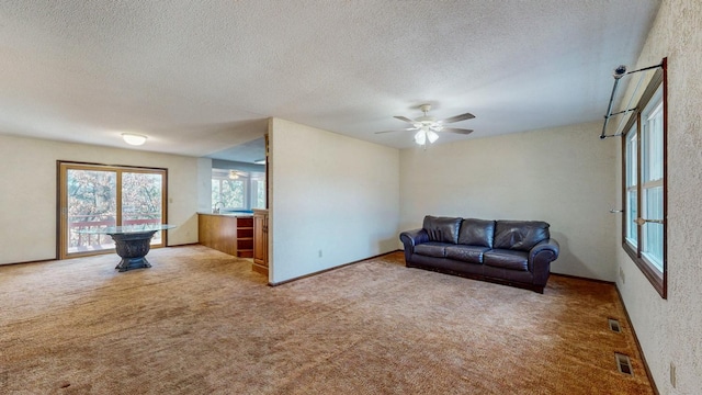 carpeted living area featuring a ceiling fan, visible vents, and a textured ceiling