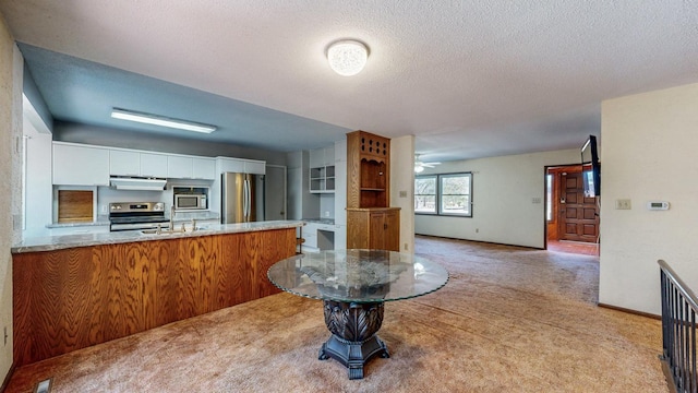 kitchen featuring range hood, appliances with stainless steel finishes, white cabinets, a peninsula, and light colored carpet