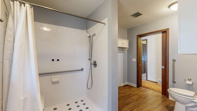 full bath featuring a tile shower, visible vents, toilet, and wood finished floors