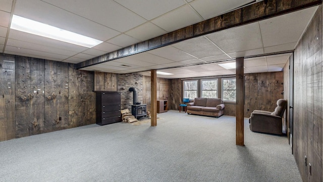 basement with a wood stove, a drop ceiling, carpet, and wood walls