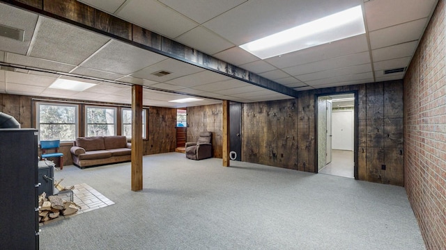 basement with carpet flooring, a drop ceiling, visible vents, and wood walls