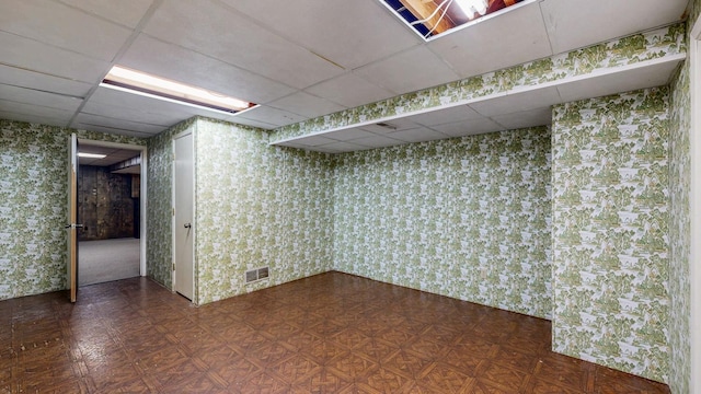 finished basement featuring tile patterned floors, visible vents, and a drop ceiling