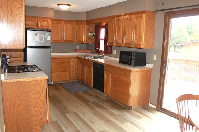 kitchen featuring black appliances, a sink, light wood-style floors, brown cabinetry, and light countertops