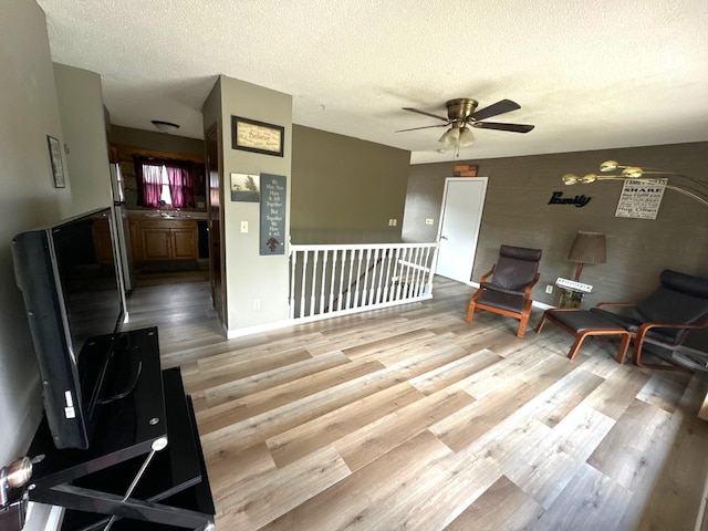 sitting room featuring light wood-type flooring, an upstairs landing, a ceiling fan, a textured ceiling, and baseboards