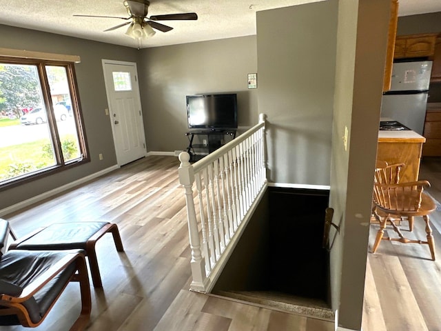 foyer featuring baseboards, a textured ceiling, light wood-style flooring, and a ceiling fan