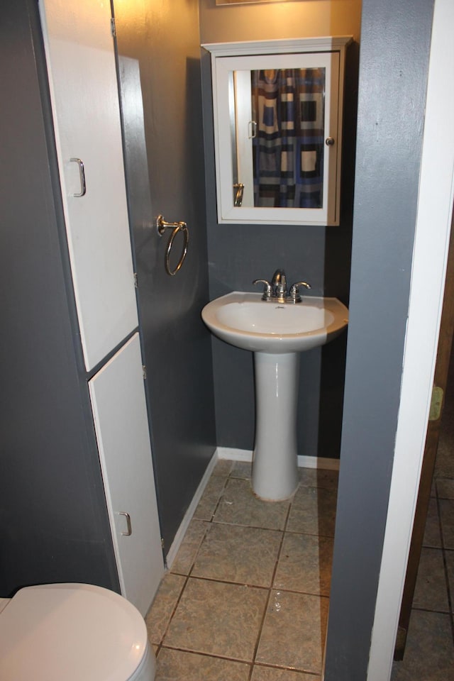 half bathroom with a sink, baseboards, toilet, and tile patterned flooring