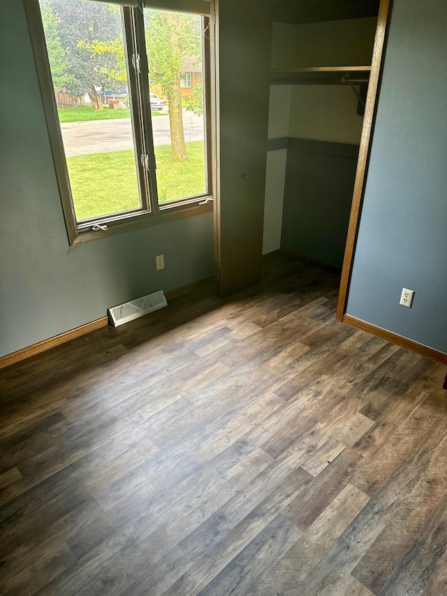 unfurnished bedroom featuring wood finished floors, visible vents, a closet, and baseboards