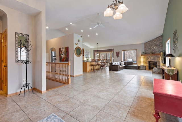 interior space featuring light tile patterned floors, high vaulted ceiling, arched walkways, a stone fireplace, and ceiling fan with notable chandelier