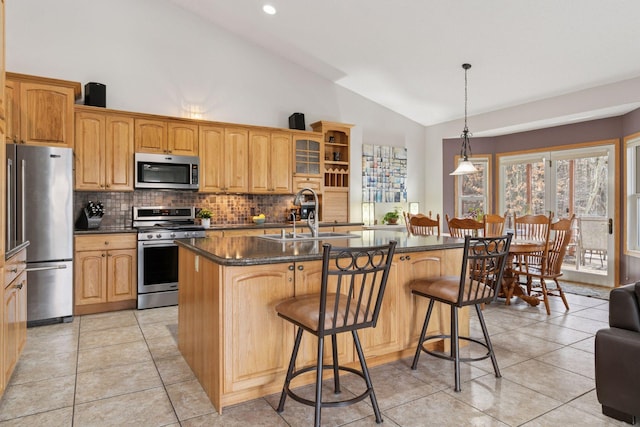 kitchen with an island with sink, a sink, stainless steel appliances, a kitchen bar, and dark countertops