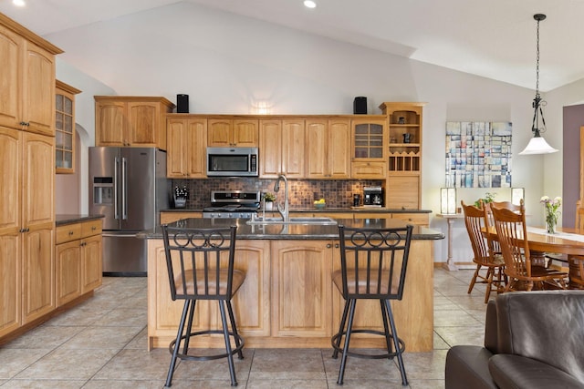 kitchen with a breakfast bar, a sink, dark countertops, appliances with stainless steel finishes, and glass insert cabinets