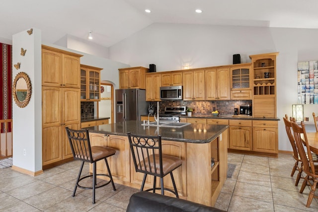 kitchen featuring decorative backsplash, open shelves, a kitchen island with sink, and stainless steel appliances