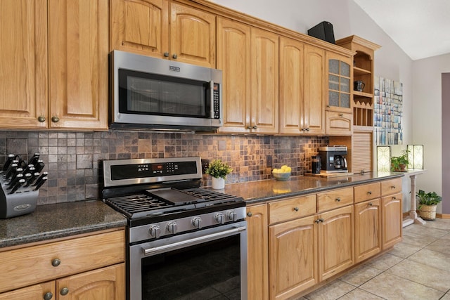 kitchen featuring lofted ceiling, light tile patterned floors, decorative backsplash, dark stone countertops, and appliances with stainless steel finishes