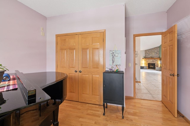 office area featuring baseboards, a textured ceiling, light wood-style flooring, and a fireplace