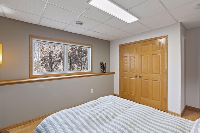 bedroom featuring wood finished floors, visible vents, baseboards, a drop ceiling, and a closet