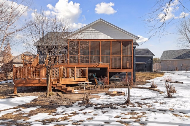 snow covered house featuring stairs, a wooden deck, a sunroom, and an outdoor fire pit