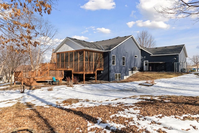 snow covered back of property with a deck and a sunroom