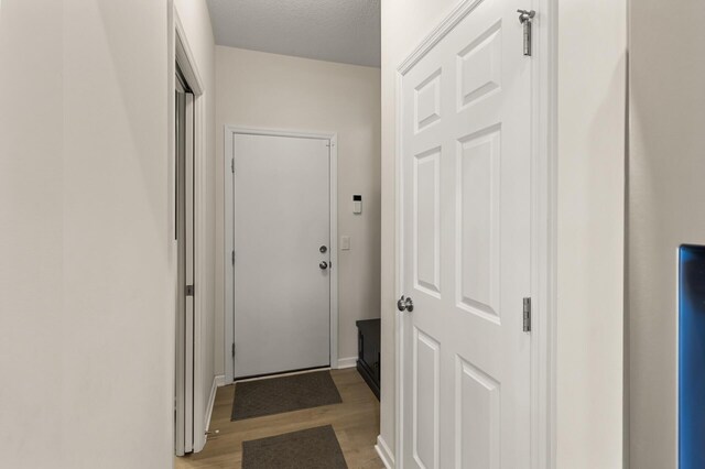 entryway with light wood finished floors, a textured ceiling, and baseboards