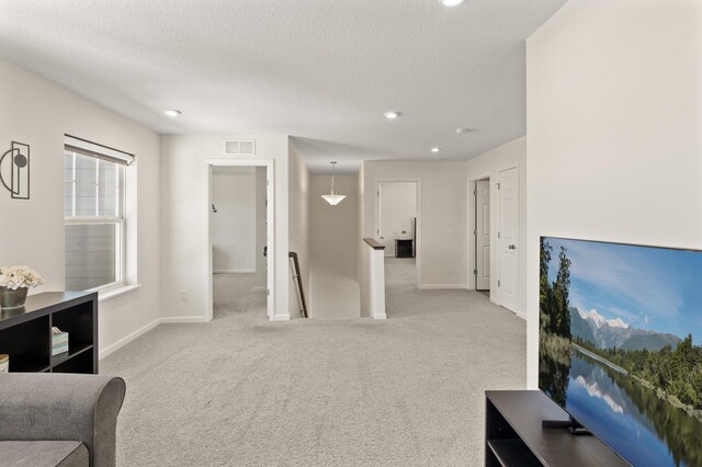 carpeted living area with visible vents, a textured ceiling, and baseboards