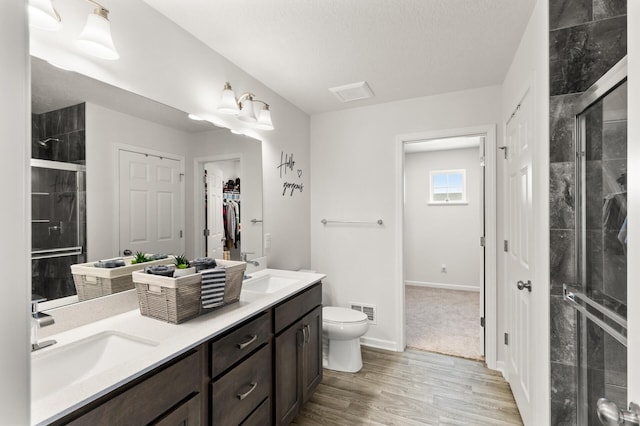 full bathroom featuring visible vents, toilet, a sink, a shower stall, and double vanity