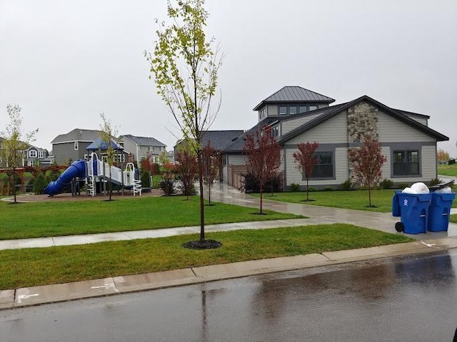 view of front of home with a front yard, a standing seam roof, concrete driveway, a garage, and a playground