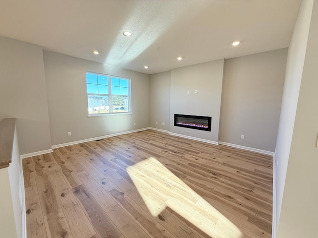 unfurnished living room featuring recessed lighting, light wood-style flooring, baseboards, and a glass covered fireplace