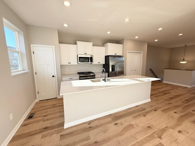 kitchen with a center island with sink, light wood-style flooring, a sink, stainless steel appliances, and white cabinetry