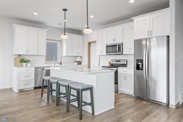 kitchen with a kitchen island, light countertops, white cabinets, light wood-style flooring, and appliances with stainless steel finishes