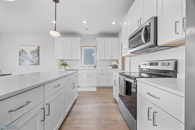 kitchen featuring decorative light fixtures, light wood-type flooring, light countertops, white cabinets, and stainless steel appliances