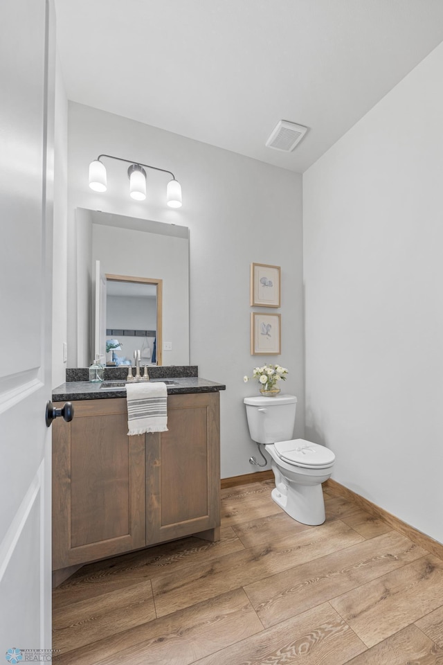half bath with vanity, wood finished floors, visible vents, and toilet