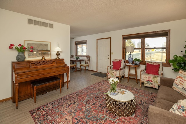 living room featuring visible vents, baseboards, a textured ceiling, and wood finished floors