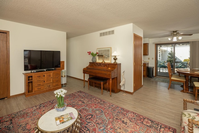 living room with visible vents, a textured ceiling, ceiling fan, and light wood finished floors