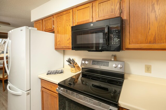 kitchen featuring black microwave, stainless steel electric range oven, light countertops, brown cabinets, and freestanding refrigerator