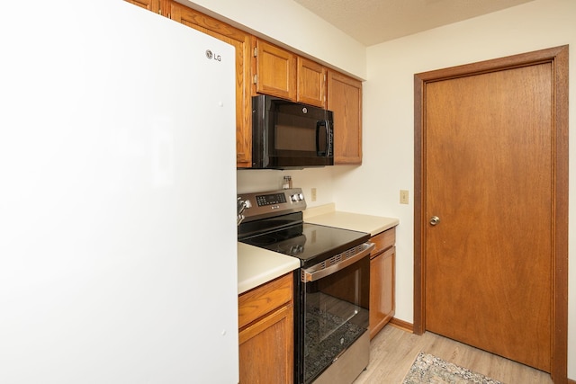 kitchen featuring light wood finished floors, stainless steel range with electric stovetop, freestanding refrigerator, black microwave, and light countertops