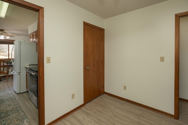 empty room featuring baseboards, a textured ceiling, a ceiling fan, and light wood finished floors