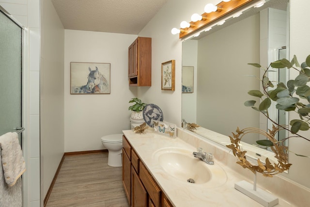 bathroom with baseboards, toilet, vanity, wood finished floors, and a textured ceiling