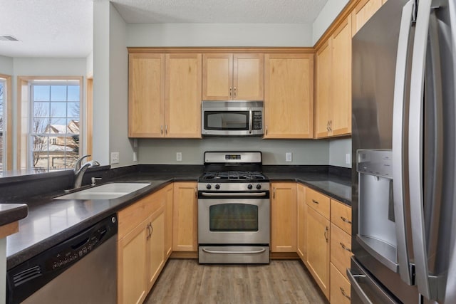 kitchen with dark countertops, light wood finished floors, a textured ceiling, stainless steel appliances, and a sink