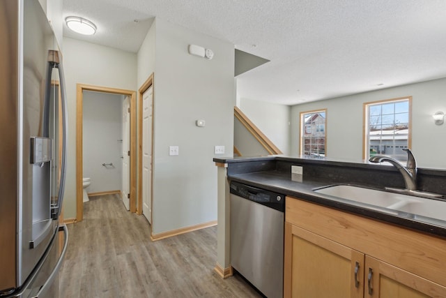 kitchen featuring dark countertops, stainless steel appliances, light wood-style floors, a textured ceiling, and a sink