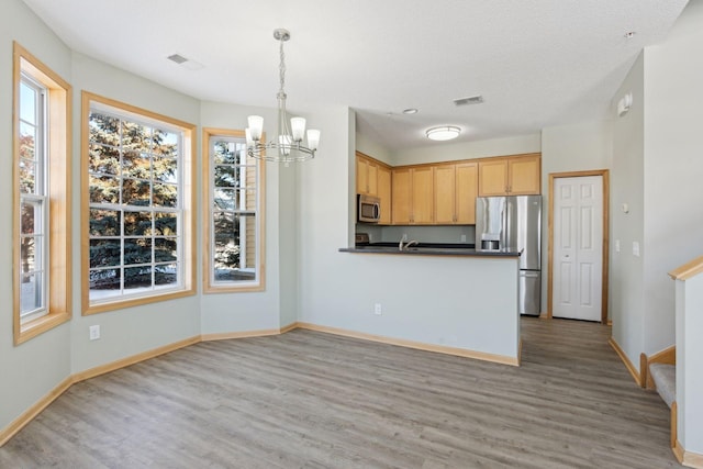 kitchen with dark countertops, a notable chandelier, appliances with stainless steel finishes, and light wood-style floors