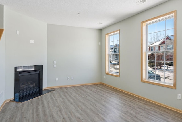 unfurnished living room featuring wood finished floors, visible vents, baseboards, a fireplace with flush hearth, and a textured ceiling