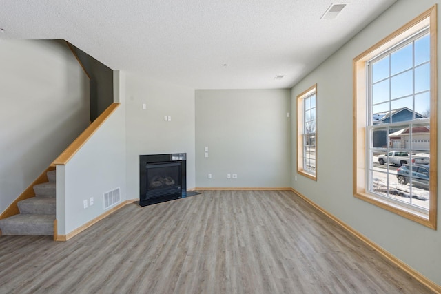 unfurnished living room with stairway, a fireplace with flush hearth, wood finished floors, and visible vents