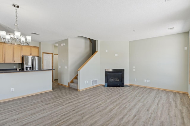 unfurnished living room with stairway, baseboards, visible vents, a notable chandelier, and light wood-type flooring