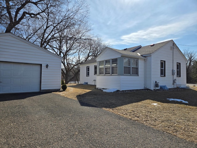 view of side of property featuring an outbuilding, driveway, a garage, and roof with shingles