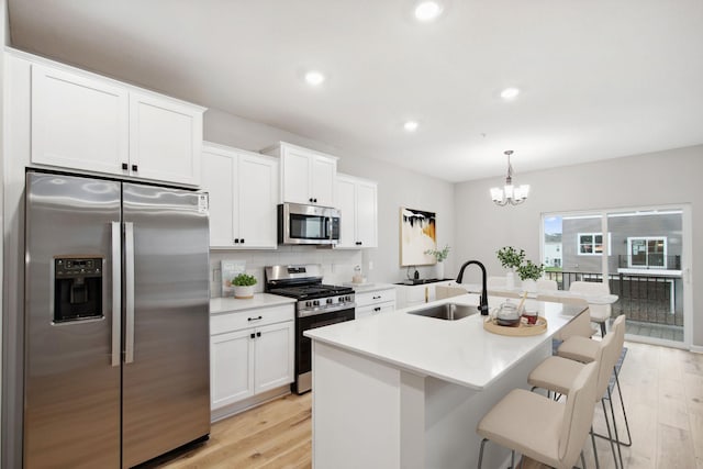 kitchen with a sink, appliances with stainless steel finishes, light wood-style floors, and a kitchen bar