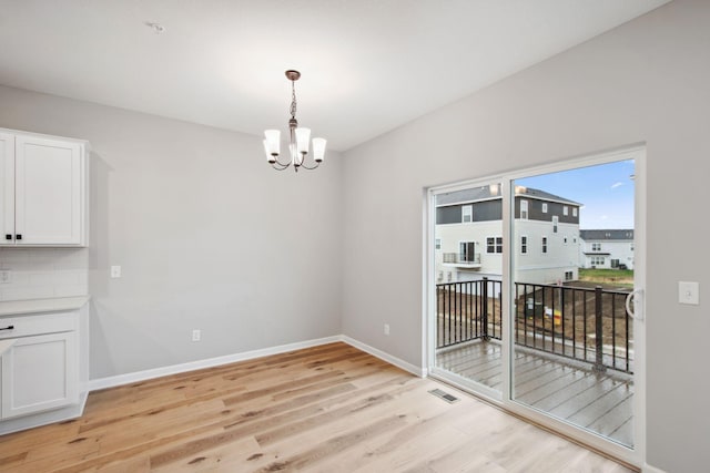 unfurnished dining area with visible vents, baseboards, an inviting chandelier, and light wood finished floors