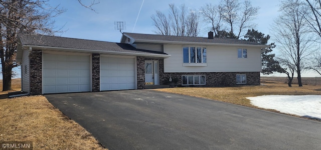 split level home featuring aphalt driveway, an attached garage, a front yard, and a chimney