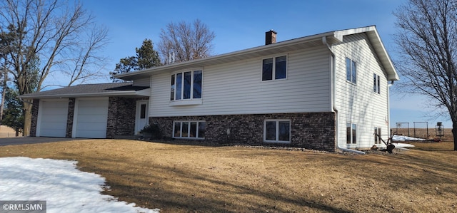 tri-level home with brick siding, an attached garage, a front lawn, a chimney, and driveway