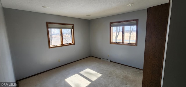 carpeted spare room featuring visible vents, a textured ceiling, and baseboards