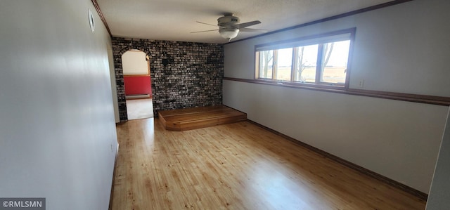 spare room featuring a ceiling fan, wood finished floors, arched walkways, and brick wall