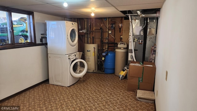 clothes washing area featuring heating unit, baseboards, laundry area, stacked washer / drying machine, and electric water heater