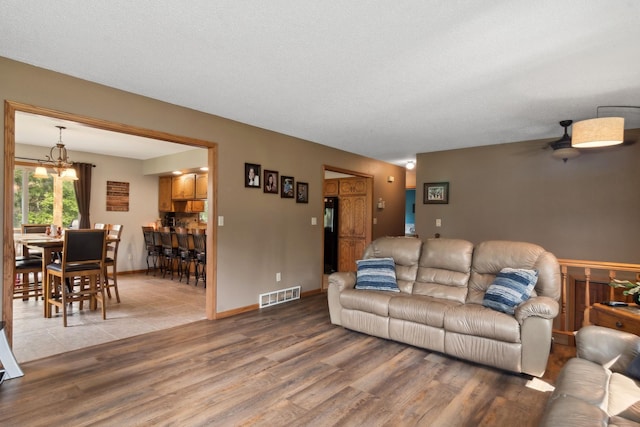 living area featuring visible vents, ceiling fan with notable chandelier, a textured ceiling, wood finished floors, and baseboards